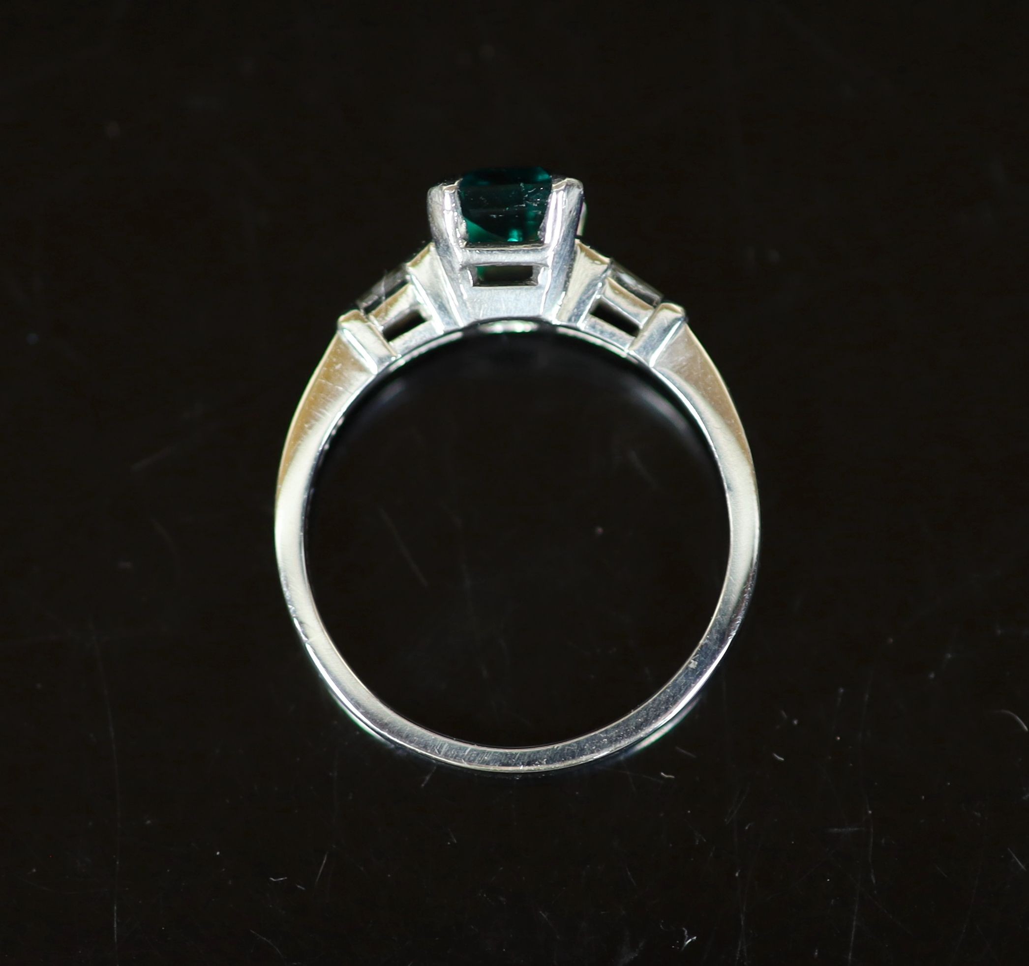 A platinum and single stone emerald ring with trapeze cut diamond set shoulders